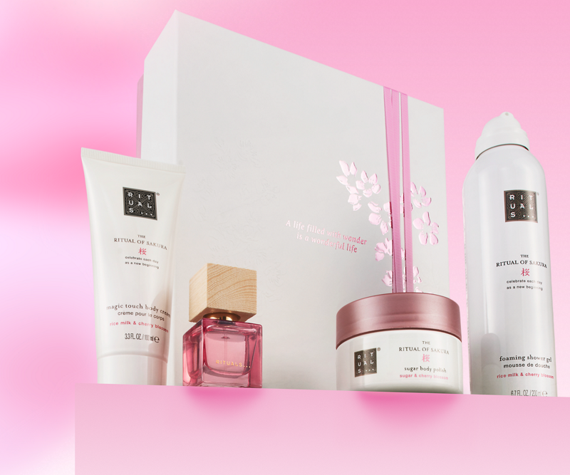 Set cadou Rituals The Ritual of Sakura cu cremă de corp, gel de duș spumant, exfoliant și parfum, prezentate pe fundal roz.